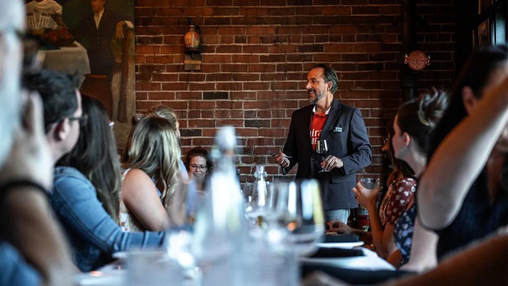 A standing toast leader with a glass, surrounded by listeners.