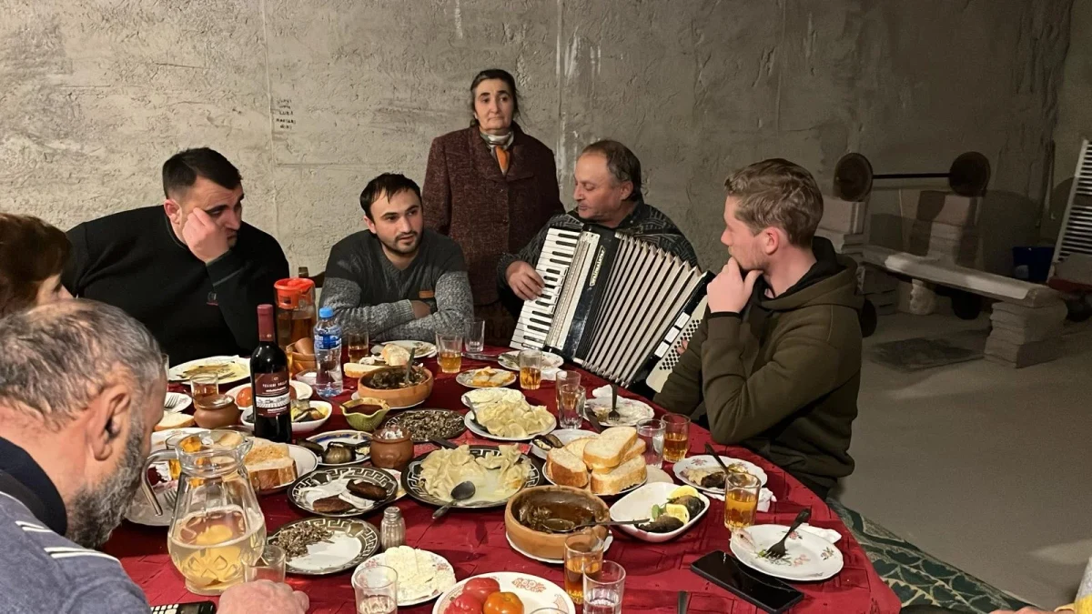 People gather around a table of shared dishes while a man plays an accordion.