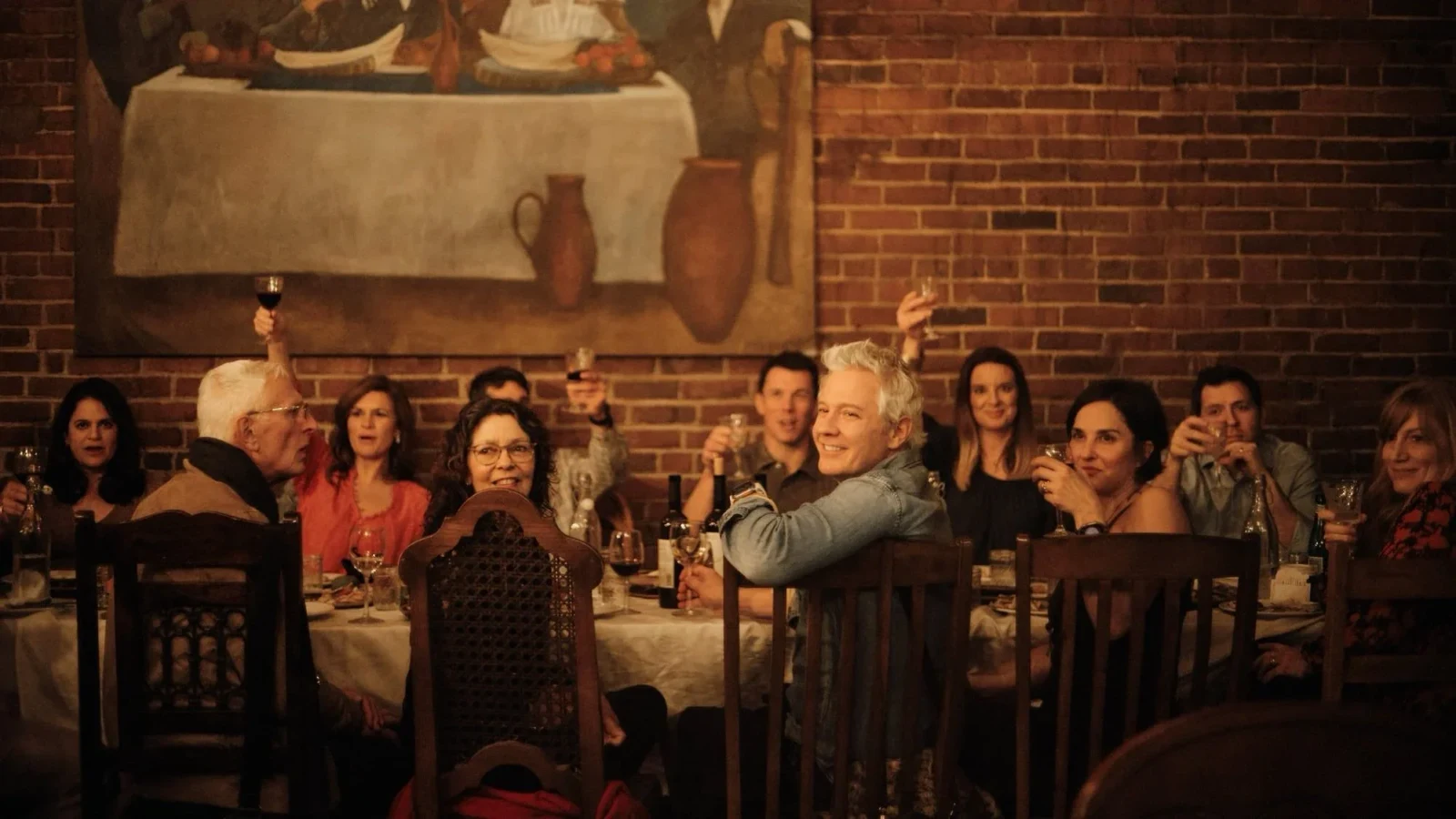Guests of different ages raise glasses around a crowded dinner table.