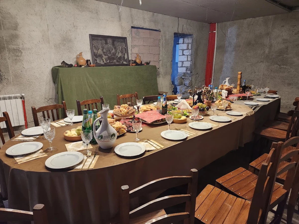 An empty table set with plates, glasses and shared dishes, surrounded by wooden chairs.